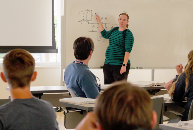 female instructor pointing at whiteboard while students watch